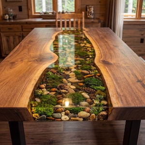 May include: A handcrafted wooden dining table with a river of clear resin filled with stones, moss, and pinecones. The table has a natural wood grain finish and black metal legs. The table is approximately 96 inches long.