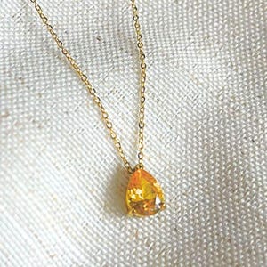 Peut inclure: Un collier à chaîne fine de couleur dorée orné d'un pendentif unique en forme de poire, composé d'une pierre précieuse jaune à facettes. Le pendentif est suspendu à une fine chaîne en métal poli, formant un bijou simple aux tons chauds.