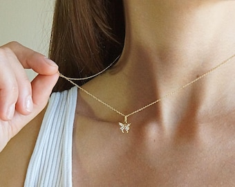 Pode incluir: Um delicado colar de ouro com um pingente de borboleta adornado com pequenas pedras preciosas brilhantes. O pingente de borboleta é suspenso por uma fina corrente de ouro. O colar é usado ao redor do pescoço.
