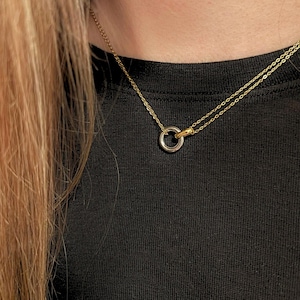 May include: A gold-toned necklace with a double chain and a small, two-tone pendant. The pendant is a circle with a silver-colored outer ring and a gold-colored inner ring. The necklace is worn against a black background.