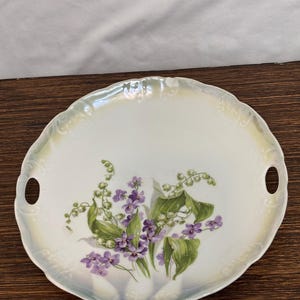 May include: A white porcelain serving plate with two handles features a floral design of purple and white flowers with green leaves.