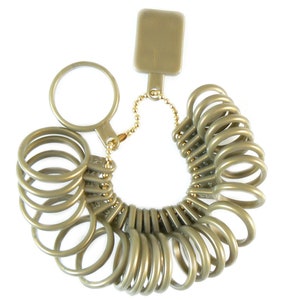 May include: A gold-colored ring sizer tool with multiple ring sizes attached to a key ring. The tool includes a small, rectangular tag and a circular handle. The ring sizes are marked with numbers.