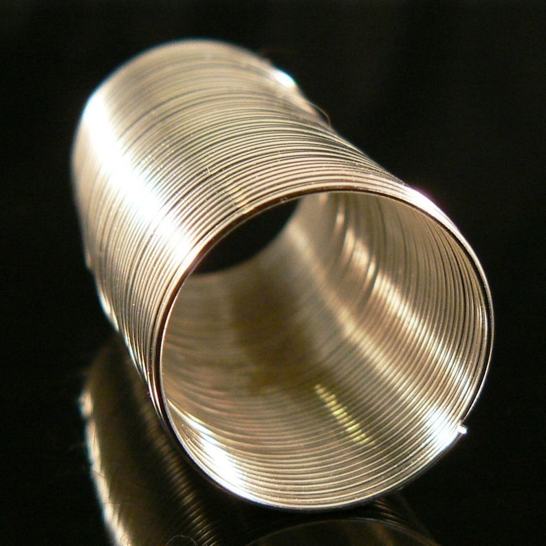 May include: A silver metal coil spring, made of many small, tightly wound rings. The spring is cylindrical in shape and has a smooth, shiny surface.