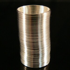 May include: A silver metal spring coil, also known as a slinky, is standing upright on a black surface.