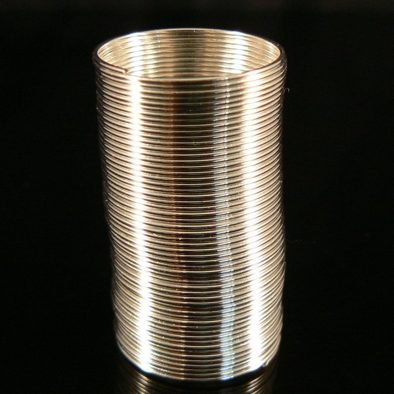 May include: A silver metal spring coil, also known as a slinky, is standing upright on a black surface.