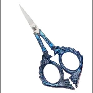 May include: Decorative embroidery scissors with a detailed blue and silver dragon scale design. The blades are silver and the handles are a gradient of blue hues. The scissors have a pointed tip and are designed for precision cutting.