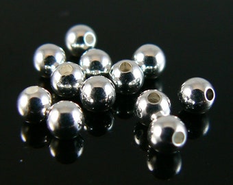 May include: A group of silver-colored metal beads, all the same size and shape, are scattered on a black surface. The beads are round and have a smooth, shiny finish.