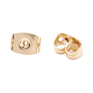 May include: Two gold-toned metal earring backs, also known as earring clutches. One piece is shown from the flat, circular front side with a central hole, and the other is shown from the side, displaying the curved, tension-based metal loops.