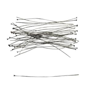 May include: A collection of thin, silver-toned metal headpins, each featuring a small flat circular head at one end. The pins are arranged in a loose, overlapping cluster, with one single pin positioned horizontally below the main group.