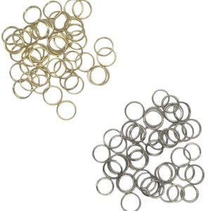 May include: Two piles of metal jump rings in gold and silver tones. The rings are small, circular, and open, suitable for jewelry making or crafts. The gold rings are clustered on the left, while the silver rings are on the right.