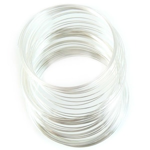 May include: A coil of silver wire, tightly wound into a circular shape. The wire is shiny and reflective, and the coils are neatly stacked on top of each other.