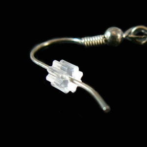 May include: Close-up of a silver earring with a clear plastic stopper. The earring is a simple hoop style with a small ball at the top.