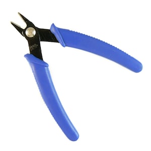 Puede incluir: Cortadores de alambre con mangos azules y una cuchilla de metal negro. Los cortadores están etiquetados como "Bead Smith".