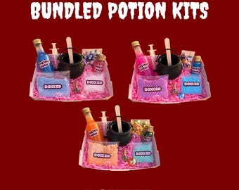 Könnte beinhalten: Drei Potion-Kits mit der Aufschrift BOXKED, die jeweils einen schwarzen Kunststoffkessel, einen Rührstab aus Holz, eine Kunststoffspritze, eine Flasche mit der Aufschrift magical water und bunte Perlen und Pailletten auf rosa Papier enthalten.