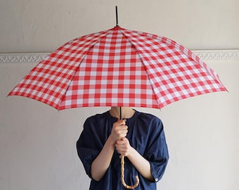 May include: A red and white gingham umbrella with a wooden handle. The umbrella is held by a person wearing a blue shirt.