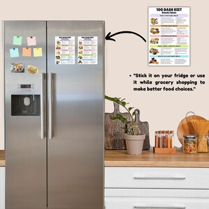 May include: A stainless steel refrigerator with two doors. A colorful printable chart with the text "100 DASH DIET Snacks Ideas" is attached to the right door with a magnet. The chart lists different snack ideas for a healthy diet.