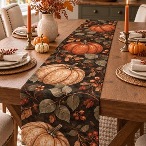 May include: A rectangular table runner featuring a dark background with a repeating pattern of orange pumpkins, green leaves, and red berries. The fabric runner is laid flat across a wooden dining table, showcasing a detailed autumnal botanical print.