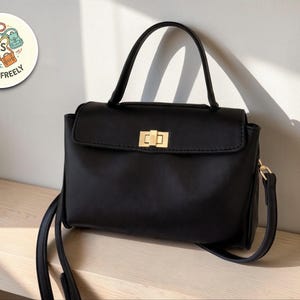 May include: A black handbag with a top handle and a detachable shoulder strap. The bag features a gold-colored clasp and a flap closure. The logo "Carry Freely" is in a circle in the upper left corner.