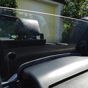 Può includere: Interni di un'auto nera con un deflettore del vento in plastica trasparente installato dietro i sedili anteriori. Il deflettore è progettato per ridurre il rumore del vento e migliorare il comfort dei passeggeri.