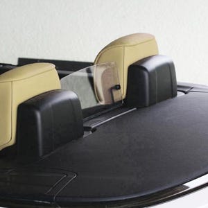 Peut inclure: Gros plan de l'intérieur arrière d'une voiture décapotable. L'image montre deux appuie-têtes beiges et des arceaux noirs. Un déflecteur de vent transparent est positionné entre les appuie-têtes. Le pont arrière de la voiture est noir.