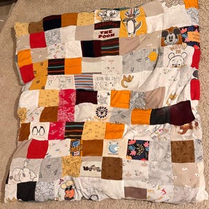 Peut inclure: Une courtepointe en patchwork réalisée à partir de différents morceaux de tissu représentant des personnages de dessins animés comme Winnie l'ourson, Mickey Mouse et un lion. La courtepointe est réalisée dans une variété de couleurs, notamment le rouge, le jaune, le marron et le blanc.