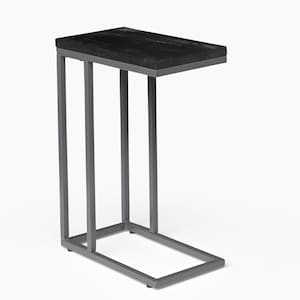 Könnte beinhalten: Ein Beistelltisch mit einer schwarzen Holzplatte und einem silbernen Metallrahmen. Der Tisch hat eine rechteckige Platte und ein C-förmiges Gestell.