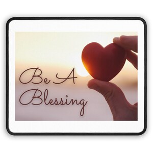 Puede incluir: Un corazón rojo sostenido en una mano contra un fondo de puesta de sol con el texto "Be A Blessing" en cursiva marrón.