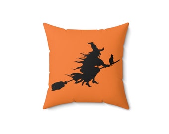 May include: Orange throw pillow with a black silhouette of a witch flying on a broomstick with a black cat.
