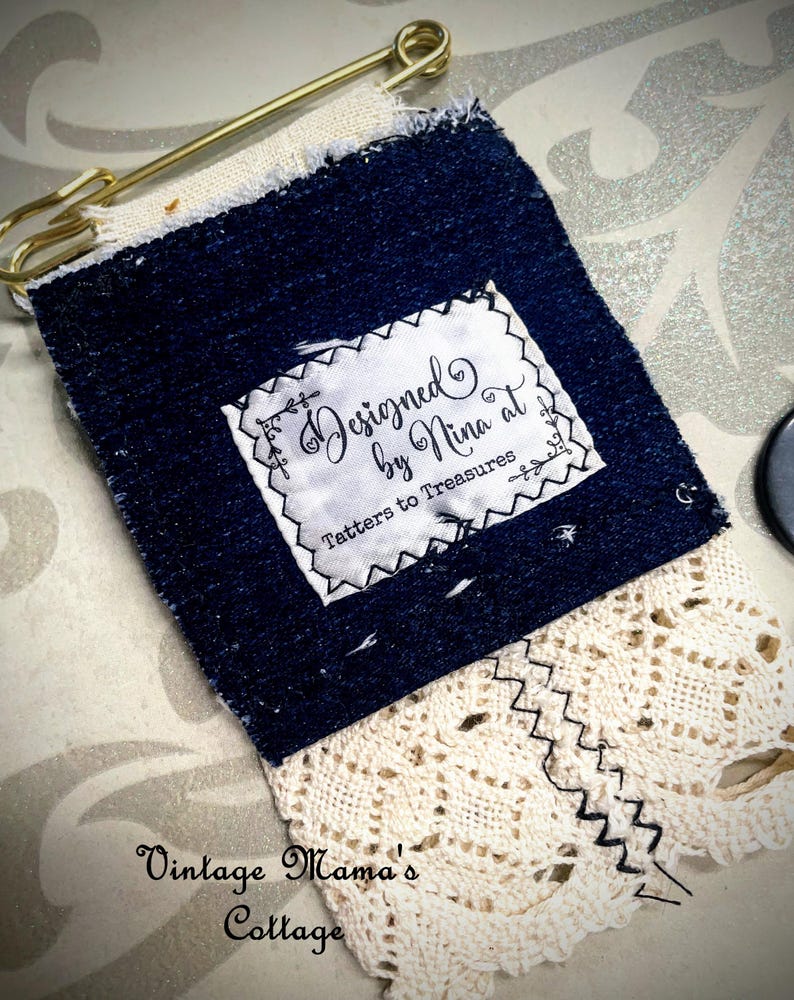 Puede incluir: Una etiqueta artesanal de mezclilla y encaje con el texto "Designed by Nina at Tatters to Treasures". La etiqueta est&aacute; asegurada con un imperdible dorado. La parte inferior de la etiqueta presenta encaje color crema con una costura en zigzag.