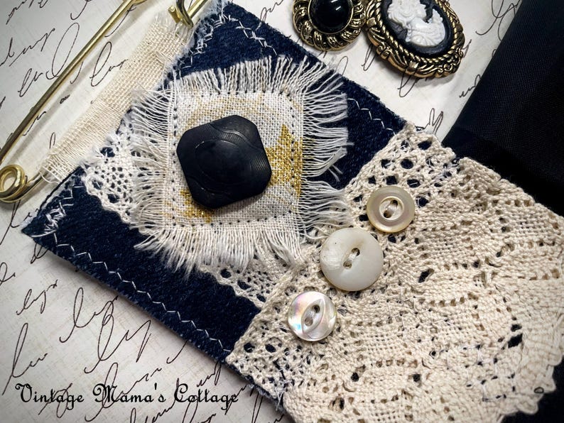 Puede incluir: Un surtido de suministros de artesan&iacute;a de estilo vintage, que incluye un parche de tela azul marino y crema con un bot&oacute;n negro, ribete de encaje y botones de n&aacute;car. Tambi&eacute;n se ven dos broches de camafeo y un imperdible dorado.