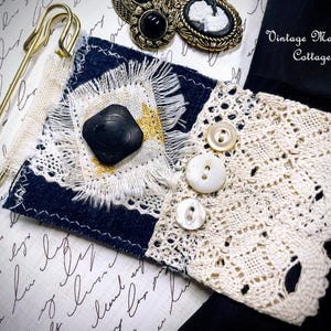 Puede incluir: Un collage de adornos de estilo vintage. Se muestra un imperdible dorado grande, un trozo de tela azul marino y blanco con un bot&oacute;n negro y un pu&ntilde;o de encaje crema con botones de perlas. Tambi&eacute;n se ven dos broches de camafeo antiguos. El texto "Vintage Mama's Cottage" es visible.