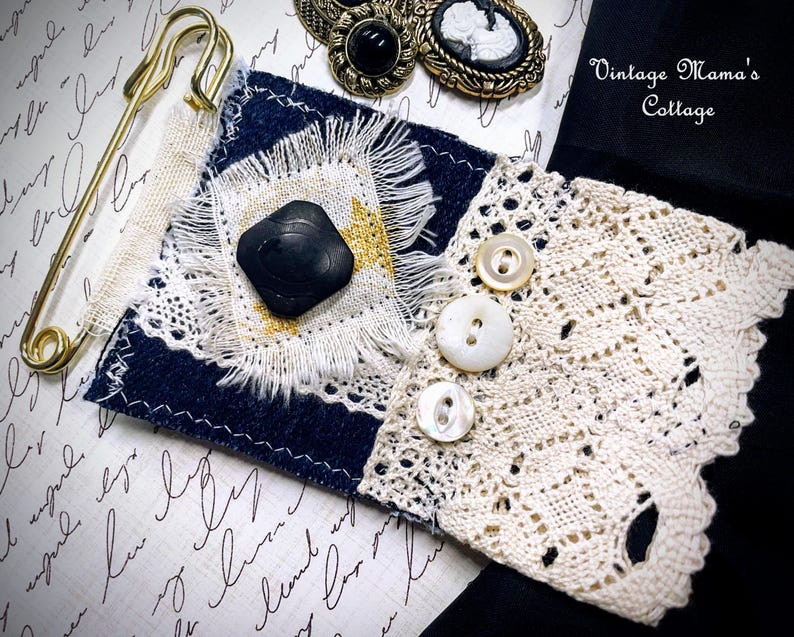 Puede incluir: Un collage de adornos de estilo vintage. Se muestra un imperdible dorado grande, un trozo de tela azul marino y blanco con un bot&oacute;n negro y un pu&ntilde;o de encaje crema con botones de perlas. Tambi&eacute;n se ven dos broches de camafeo antiguos. El texto "Vintage Mama's Cottage" es visible.