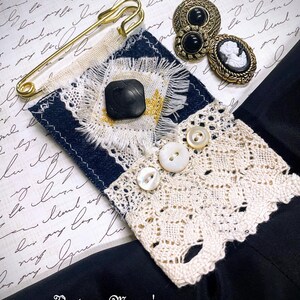 Puede incluir: Una variedad de art&iacute;culos de costura de estilo vintage, que incluyen un imperdible dorado, botones negros y un broche de camafeo. Tambi&eacute;n se presenta una pieza de tela azul marino y crema con un bot&oacute;n cuadrado negro y ribete de encaje. La imagen incluye el texto "Vintage Mama's Cottage."