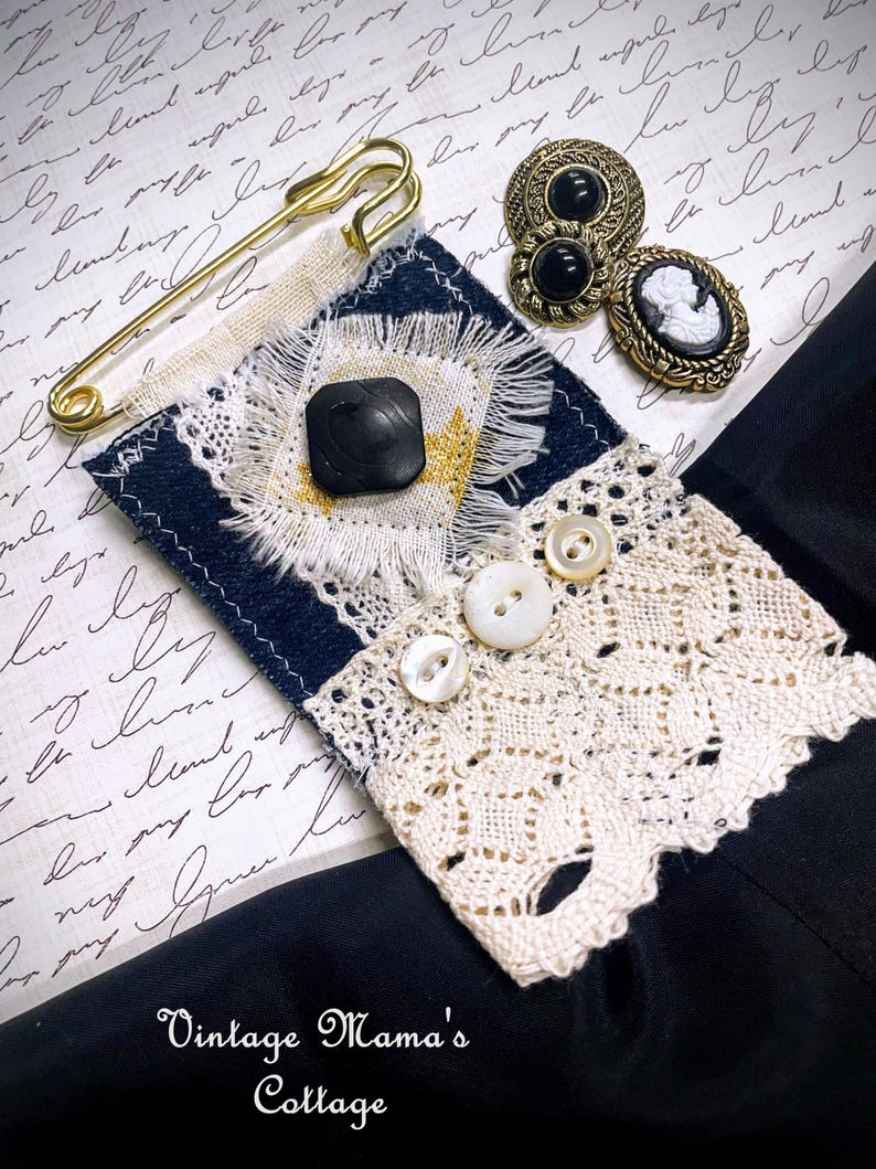 Puede incluir: Una variedad de art&iacute;culos de costura de estilo vintage, que incluyen un imperdible dorado, botones negros y un broche de camafeo. Tambi&eacute;n se presenta una pieza de tela azul marino y crema con un bot&oacute;n cuadrado negro y ribete de encaje. La imagen incluye el texto "Vintage Mama's Cottage."