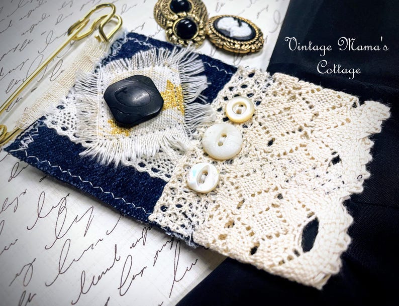 Puede incluir: Una pieza textil artesanal con mezclilla, encaje y un bot&oacute;n negro. El dise&ntilde;o incorpora un imperdible dorado, botones vintage y el texto "Vintage Mama's Cottage". La pieza muestra una mezcla de texturas y materiales.