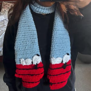 May include: Crocheted scarf featuring a light blue body with red and black striped mittens at the ends. The scarf has white and black details, and a matching light blue crocheted neck warmer.