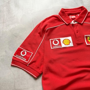 Pu&ograve; includere: Polo rosso con dettagli bianchi e colletto. Presenta i loghi Vodafone e Shell. La maglietta ha maniche corte e colletto button-down. La maglietta &egrave; realizzata in materiale morbido.