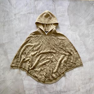 May include: A tan hooded poncho with a floral pattern. The poncho is made of a soft, knitted fabric.