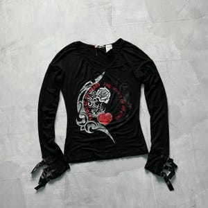May include: Black long-sleeve shirt with a v-neck and a graphic print of a rose and heart with the text "The Soul of My Mind, The Wings of My Heart". The shirt has black ties on the sleeves.