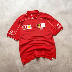 Pu&ograve; includere: Polo rosso con dettagli bianchi e loghi degli sponsor, tra cui Ferrari, Shell e Vodafone. &Egrave; presente il marchio Fila. Ha un colletto e maniche corte.