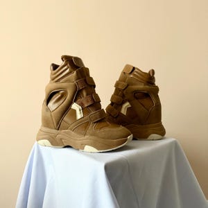 May include: A pair of brown high-top sneakers with multiple velcro straps and a chunky sole. The sneakers have a unique design with cut-out details and a mix of textures, including suede and leather-like materials.