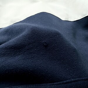May include: Close-up of a dark blue fabric with a white fabric seam. The fabric has a textured surface.