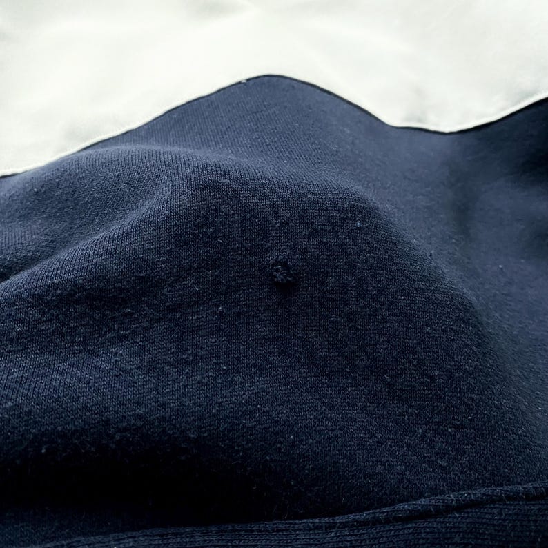 May include: Close-up of a dark blue fabric with a white fabric seam. The fabric has a textured surface.