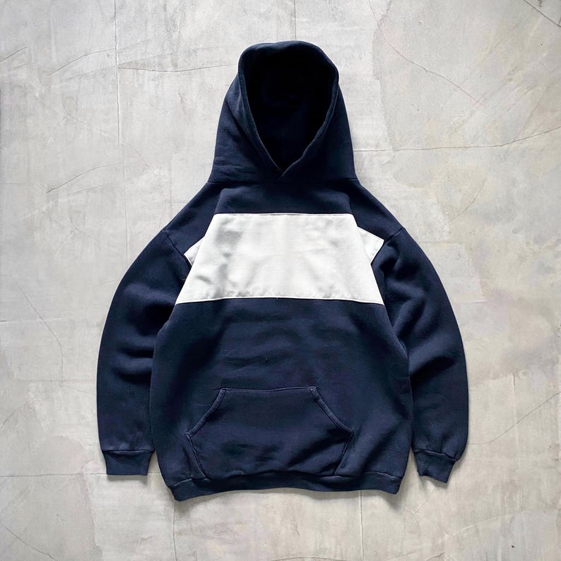 May include: A navy blue hooded sweatshirt with a white horizontal stripe across the chest. The sweatshirt has a kangaroo pocket.