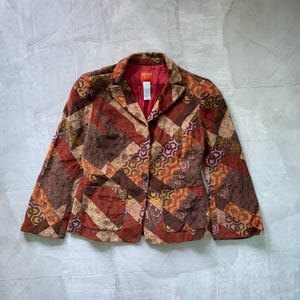 May include: A brown, red and orange patterned blazer with a button closure. The blazer has a patchwork design and a label that says "KENZO" on the inside.