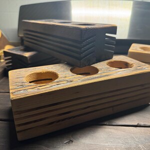 May include: A wooden stand with three circular cutouts, perfect for holding small items like essential oils or candles. The stand is made of reclaimed wood and has a rustic, weathered look.