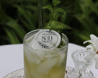 May include: A refreshing cocktail in a clear glass, garnished with mint and a decorative ice circle. The ice circle has the initials "S H" and the wedding date. A white daisy and a small glass vase are in the background.
