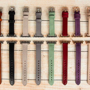 May include: Twelve different colored leather watch bands for a smart watch. The bands are all the same size and style, but they come in a variety of colors, including brown, black, gray, beige, green, red, purple, and pink.