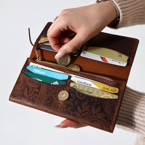 May include: A brown leather wallet with a floral embossed design. The wallet has a zipper closure and multiple card slots. It is open and has several cards and coins inside.