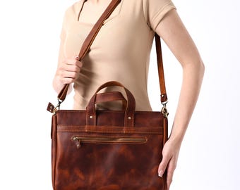 May include: A brown leather satchel bag with a top handle and a long adjustable shoulder strap. The bag has a front pocket with a zipper.